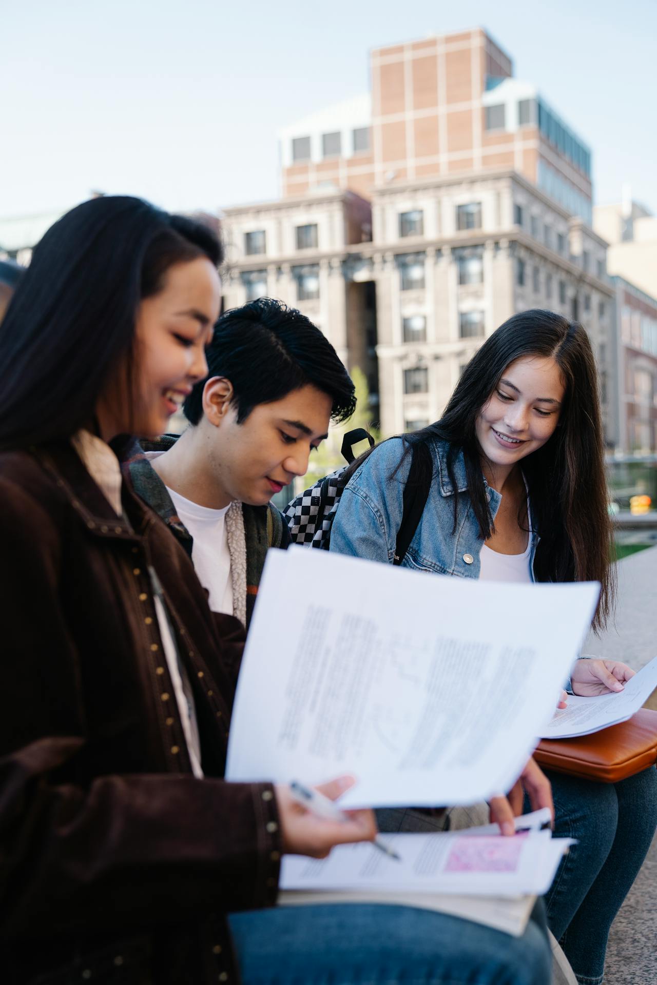 Three young college students happily sitting sharing papers with each other