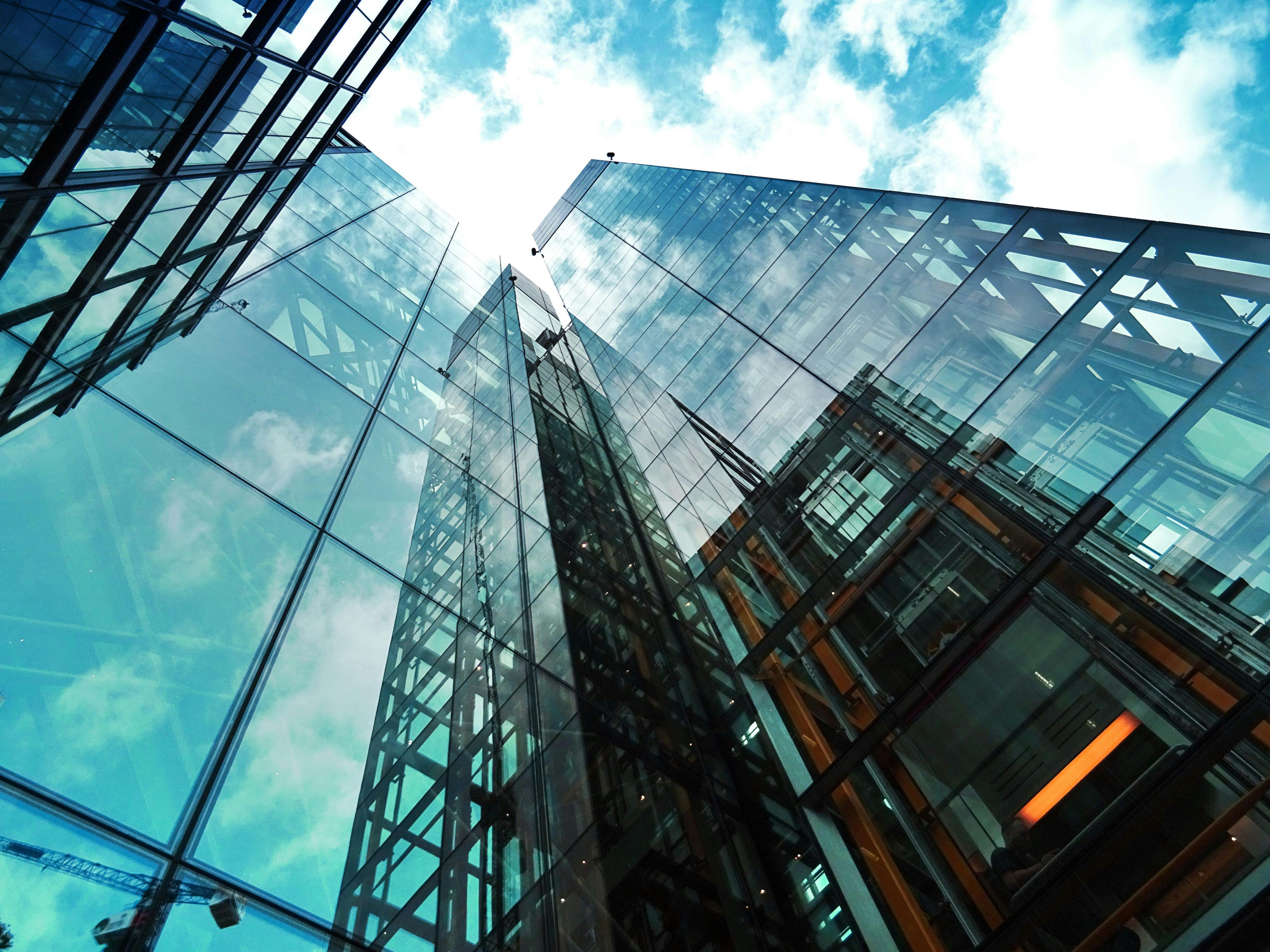 An image of a  glass walled skyscraper building reaching the sun lit blue skies above it