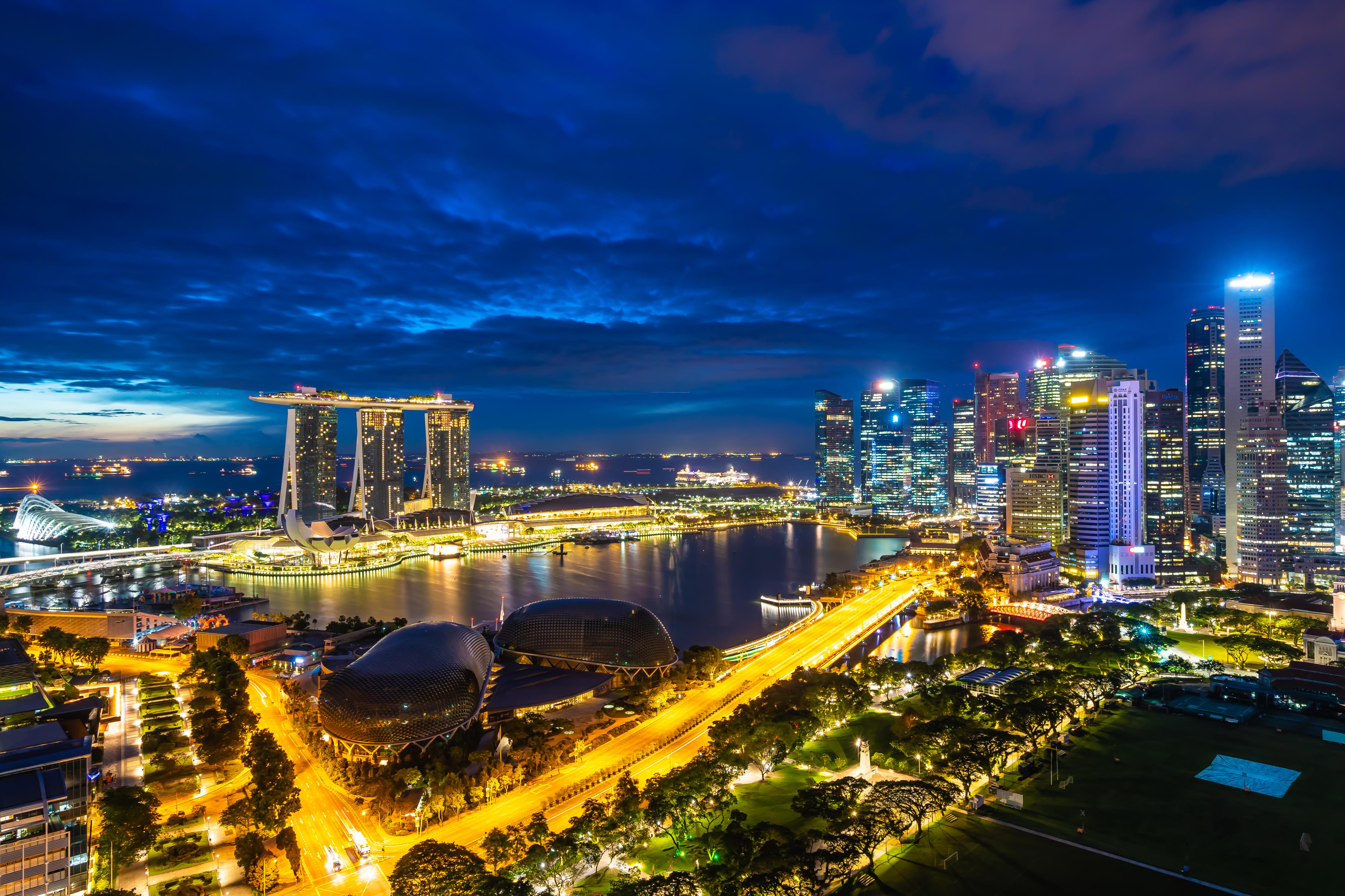 A city skyline at night with tall skyscrapers illuminated against a dark sky, reflecting on the water of a nearby lake or river. The scene captures the essence of a bustling metropolis with bright lights and urban architecture.