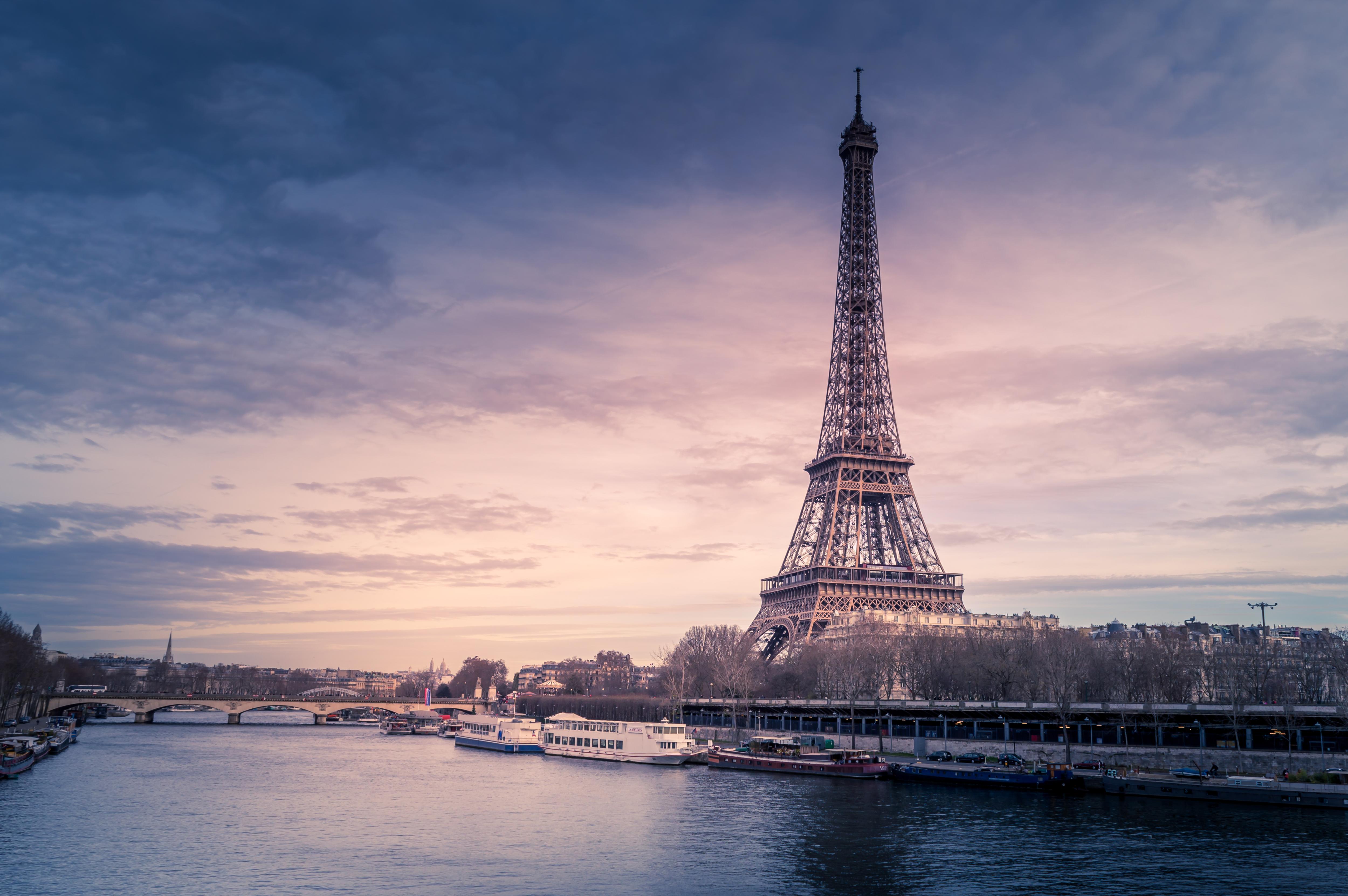 A large tower beside a body of water during sunset, with a colorful sky filled with clouds, reflecting on the lake. The scene shows a winter landscape in an urban setting.