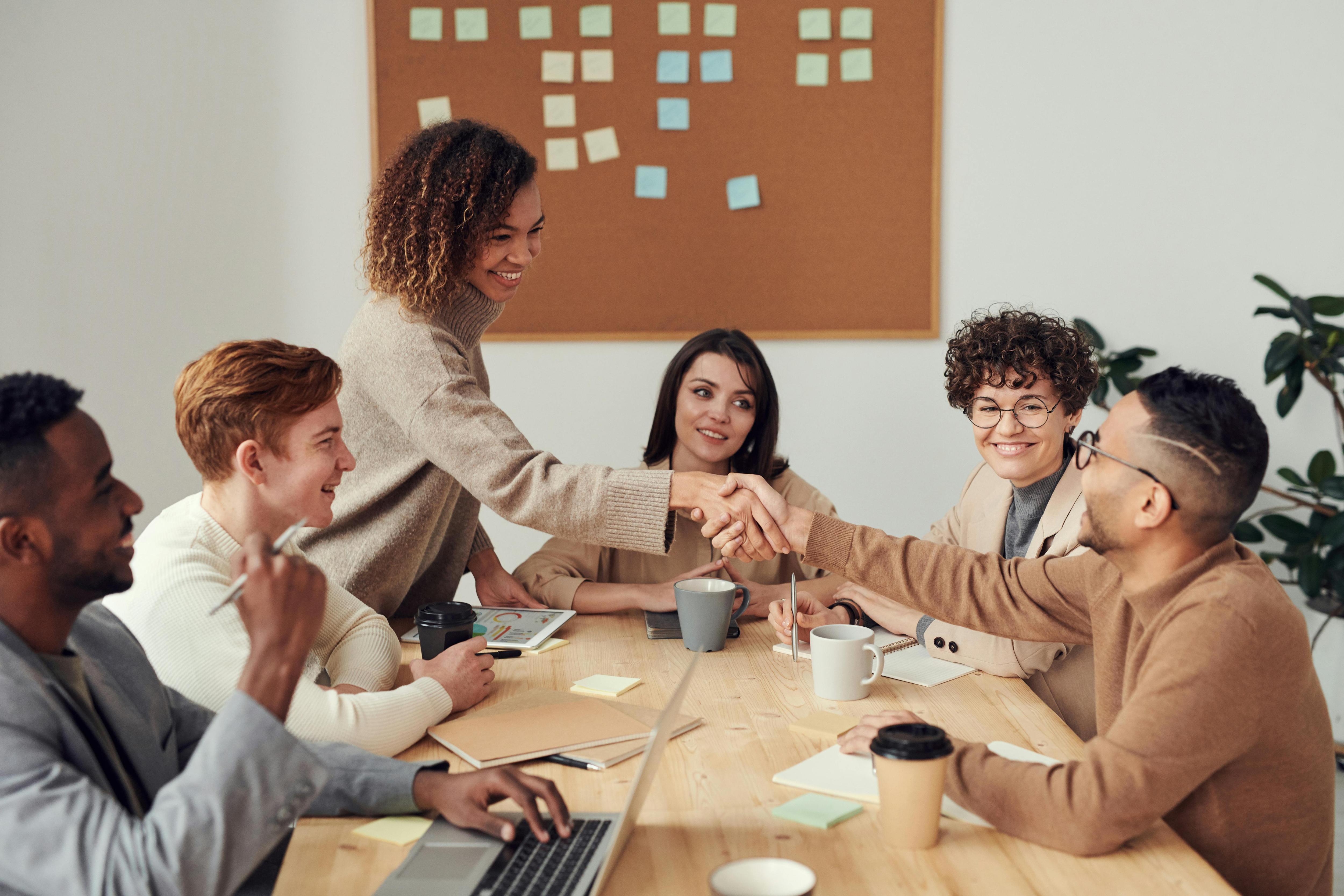 A group of young professional collaborating at a desk while one is shaking the others hand