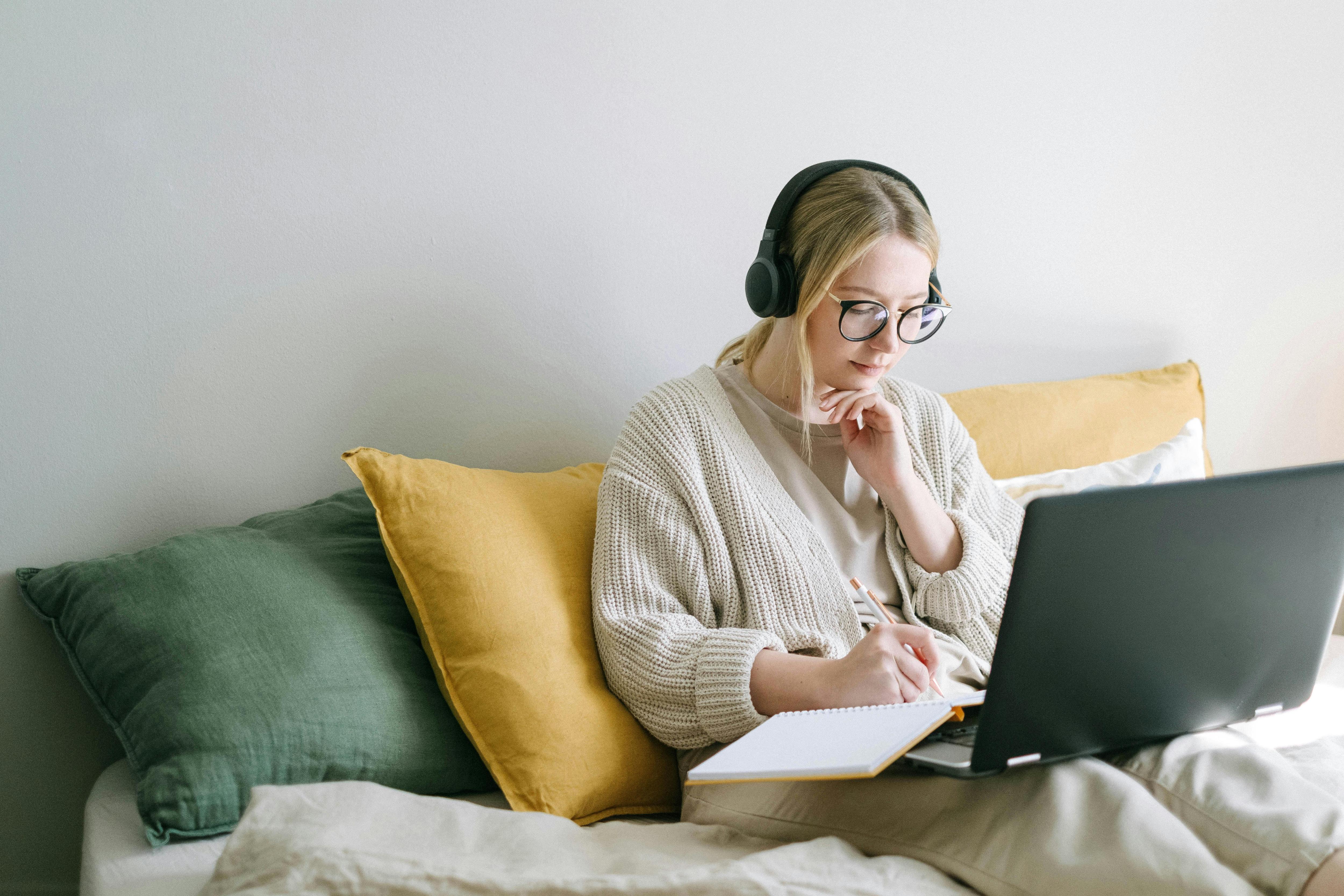 A woman sitting comfortably with her laptop resting on her legs while she listens on her headphones