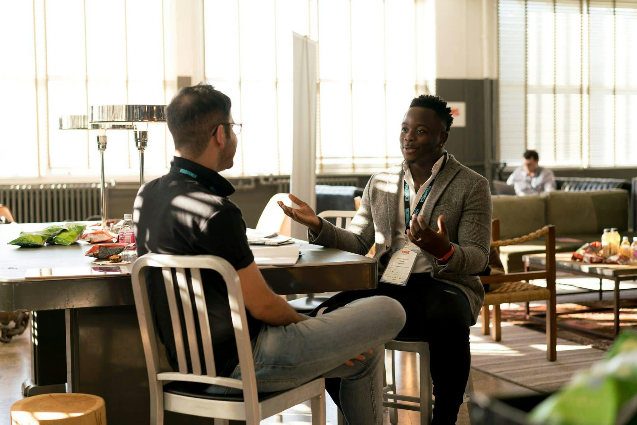 Two men sitting opposite each other leaning against a table having a happy discussion